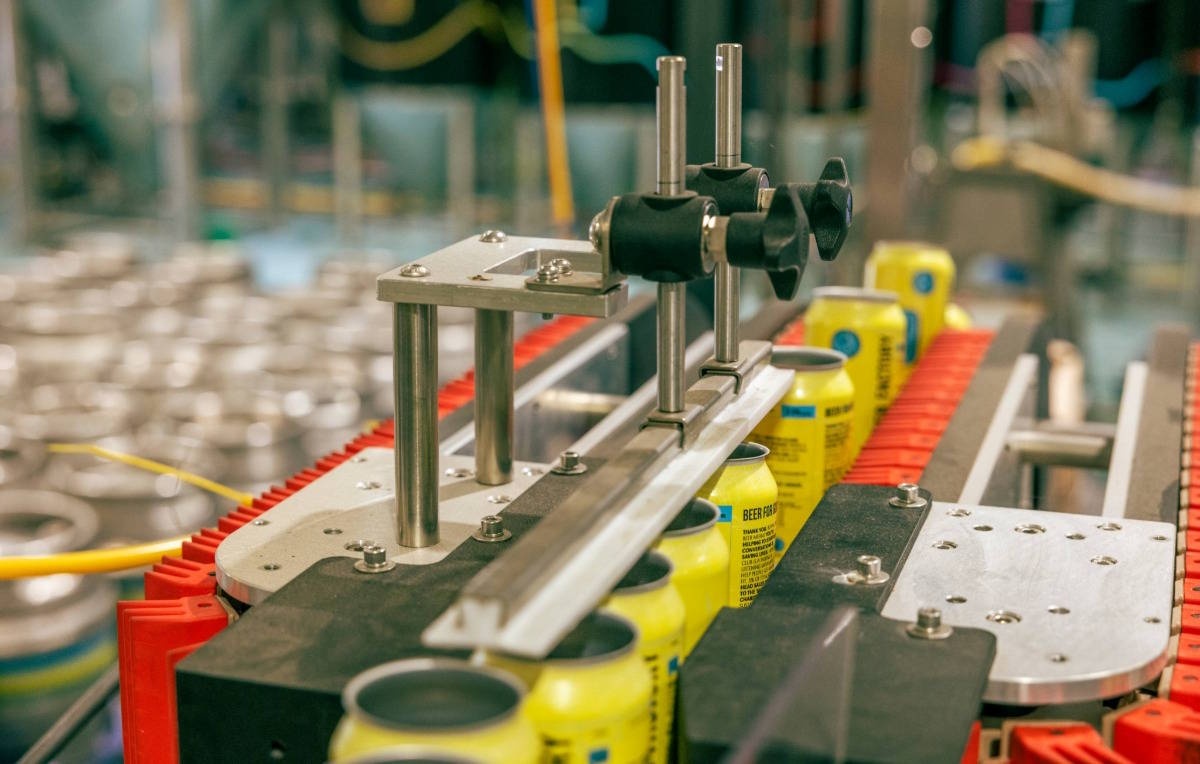 Beer cans moving along an automated canning line inside a brewery, with metal machinery guiding the cans into position.