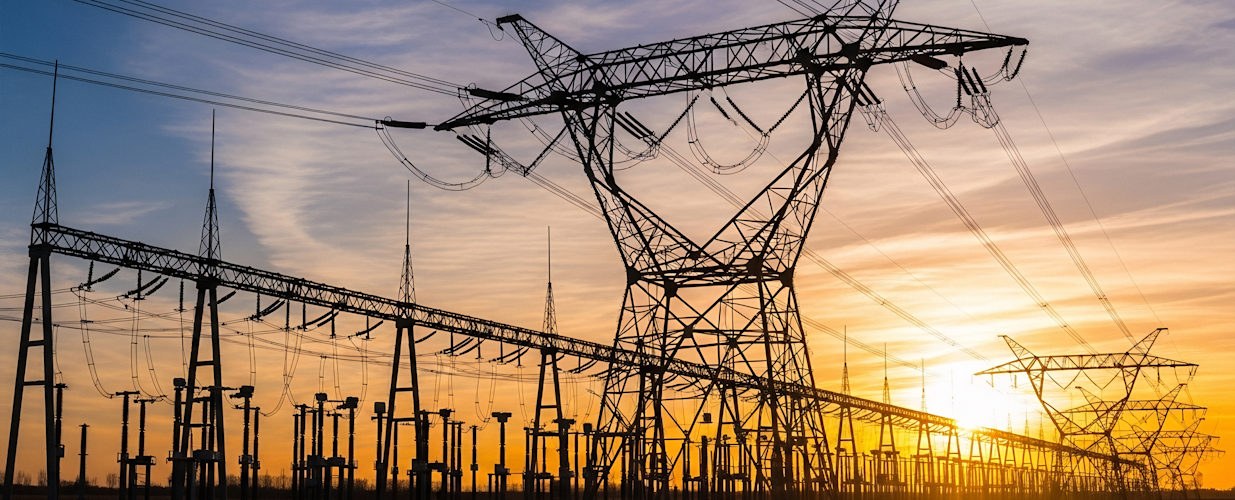 Electrical power lines and substation against a sunset or sunrise sky.