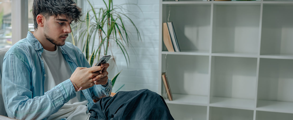A university student sits in the library using his mobile phone