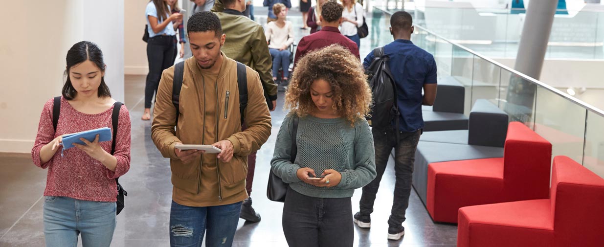 Three students walk through campus using their mobile phones