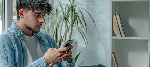A university student sits in the library using his mobile phone