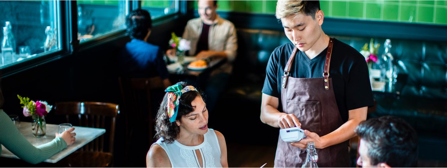 Waiter holding a handheld device, taking a card payment from a customer.