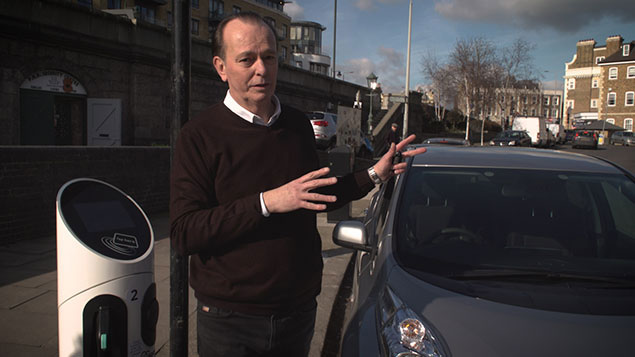 Quentin Wilson next to an electric car and charging station