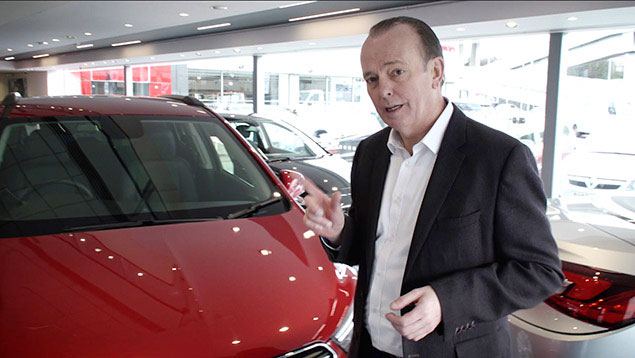 Quentin Wilson next to a red car in a car showroom