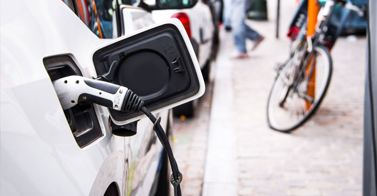 An electric charger plugged into a car parked on the road.