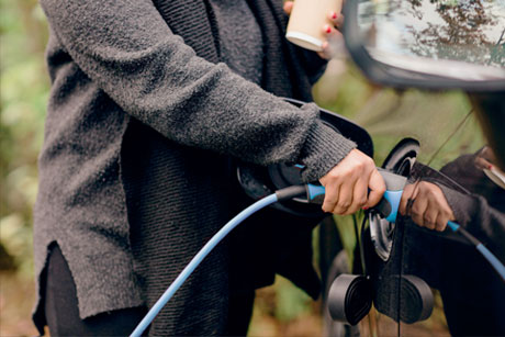 A woman plugging an electric charger into a black car.