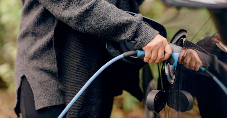 A woman plugging an electric charger into a black car.