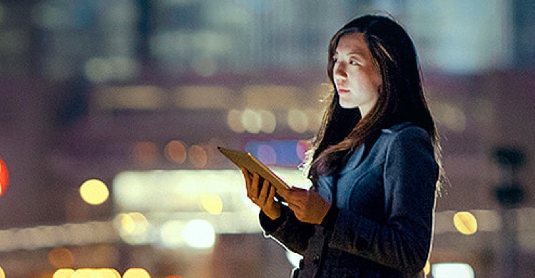 A business woman holds a tablet in a business area at night.