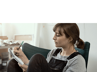 A young woman sat in an armchair writing in a notebook.