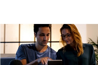 Man and woman sat on the sofa at home looking at table screen..