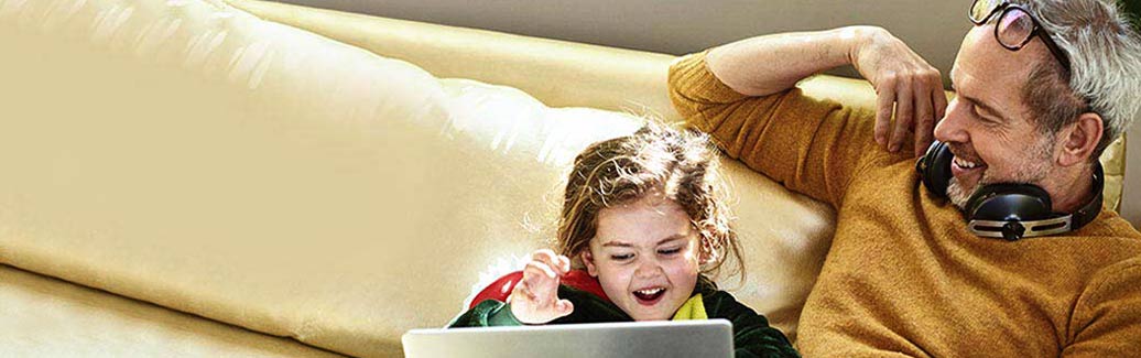 Man and young child sat on a sofa smiling. 