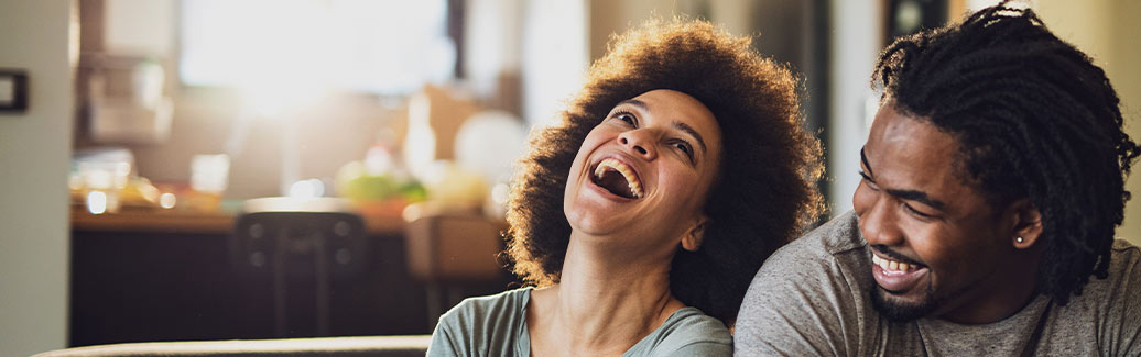 A man and woman sat at home smiling and laughing.