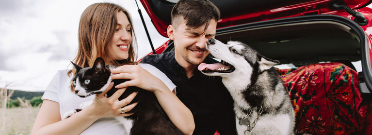 Couple holding their pets outisde the open boot of their car