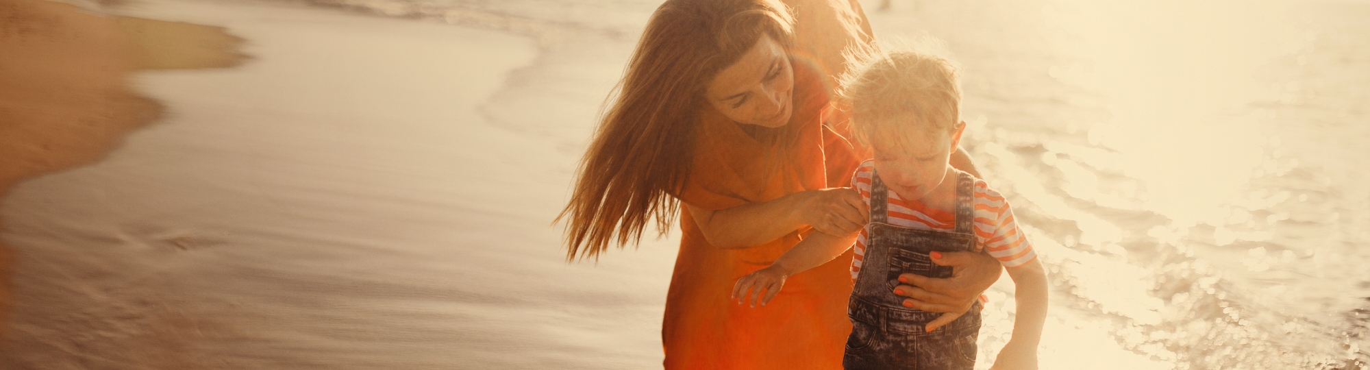 Woman and son on the beach paddling on the coastline.