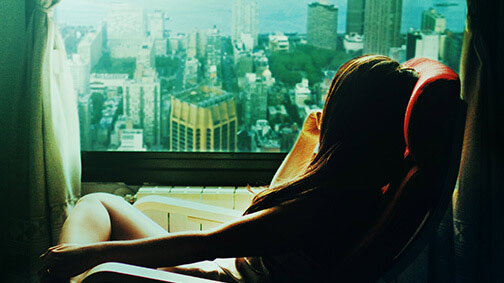 a woman peering out the window over a cityscape