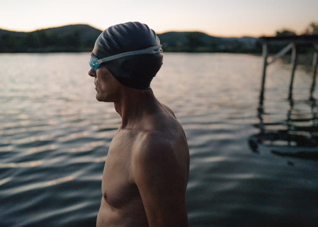 Man wearing a swimming cap stood with a river in the background