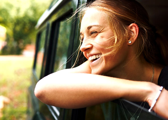Young woman smiling as she puts her head outside a movie land rover with the breeze blowing through her hair