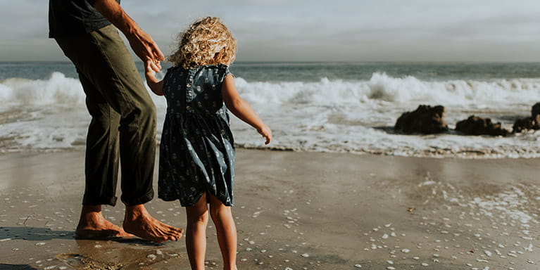 Girl and her parent holding hand and a wave comes in on the beach