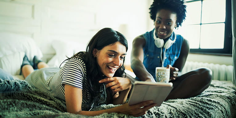 Two young women smiling as they look at an ipad