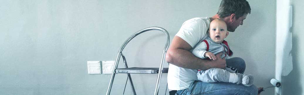 Header image of a dad with his child, roller painting a wall grey. 