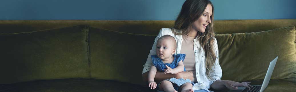 Mother holding baby whilst browsing on laptop.