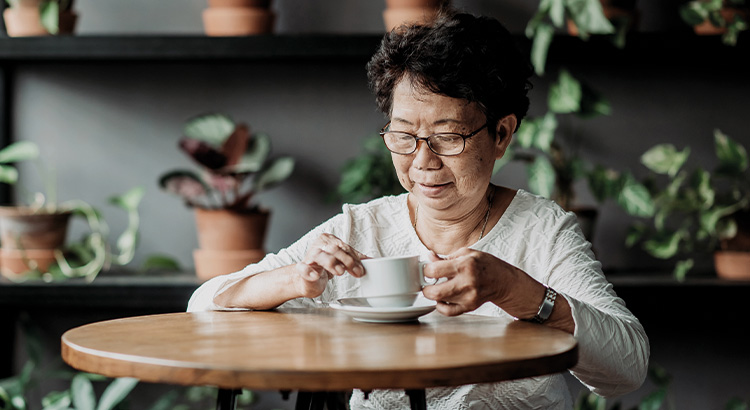 A lady holding a cup of coffee at home, with indoor plants on the shelves