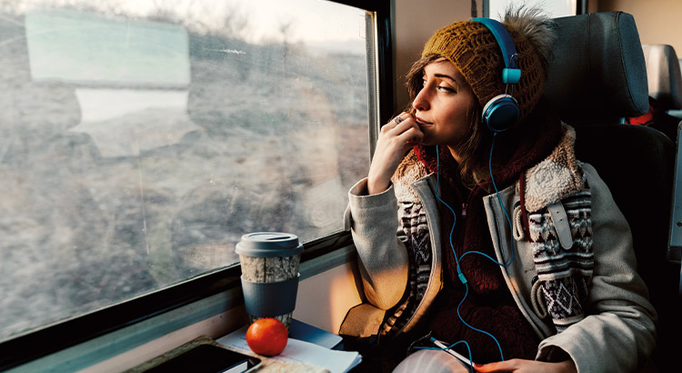 Woman looking out of a train window with headphones on