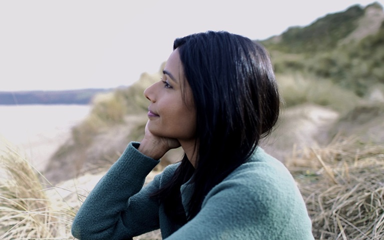 An image of a lady at the beach looking out to sea.